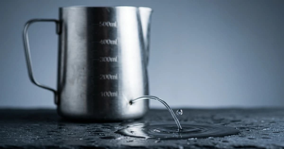 A measuring jug draining through a hole in its side, a droplet mid-fall