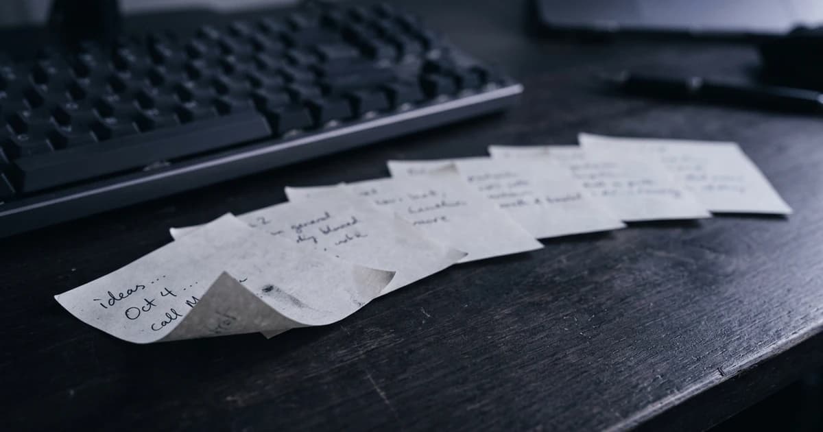 A fan of handwritten paper notes spread across a desk beside a keyboard